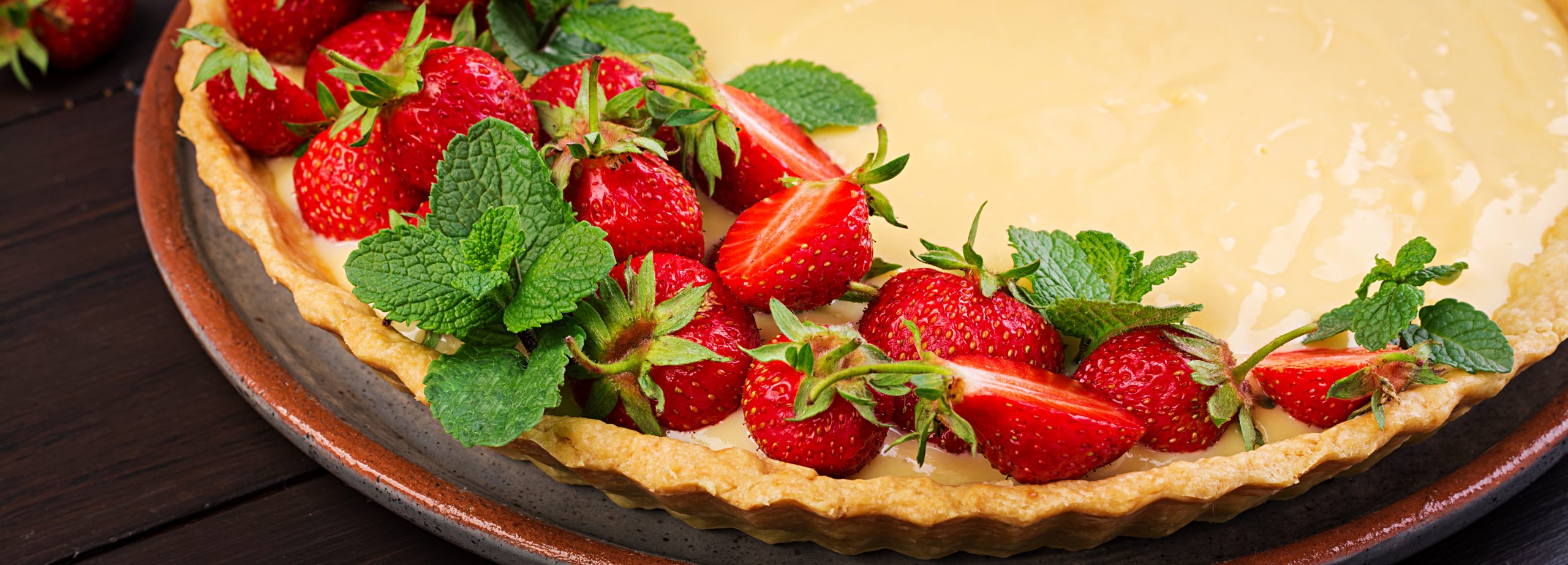 Tart with strawberries and whipped cream decorated with mint leaves on dark background. Banner
